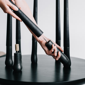 Woman placing a black 100% beeswax grove candle stick onto the holder's spike