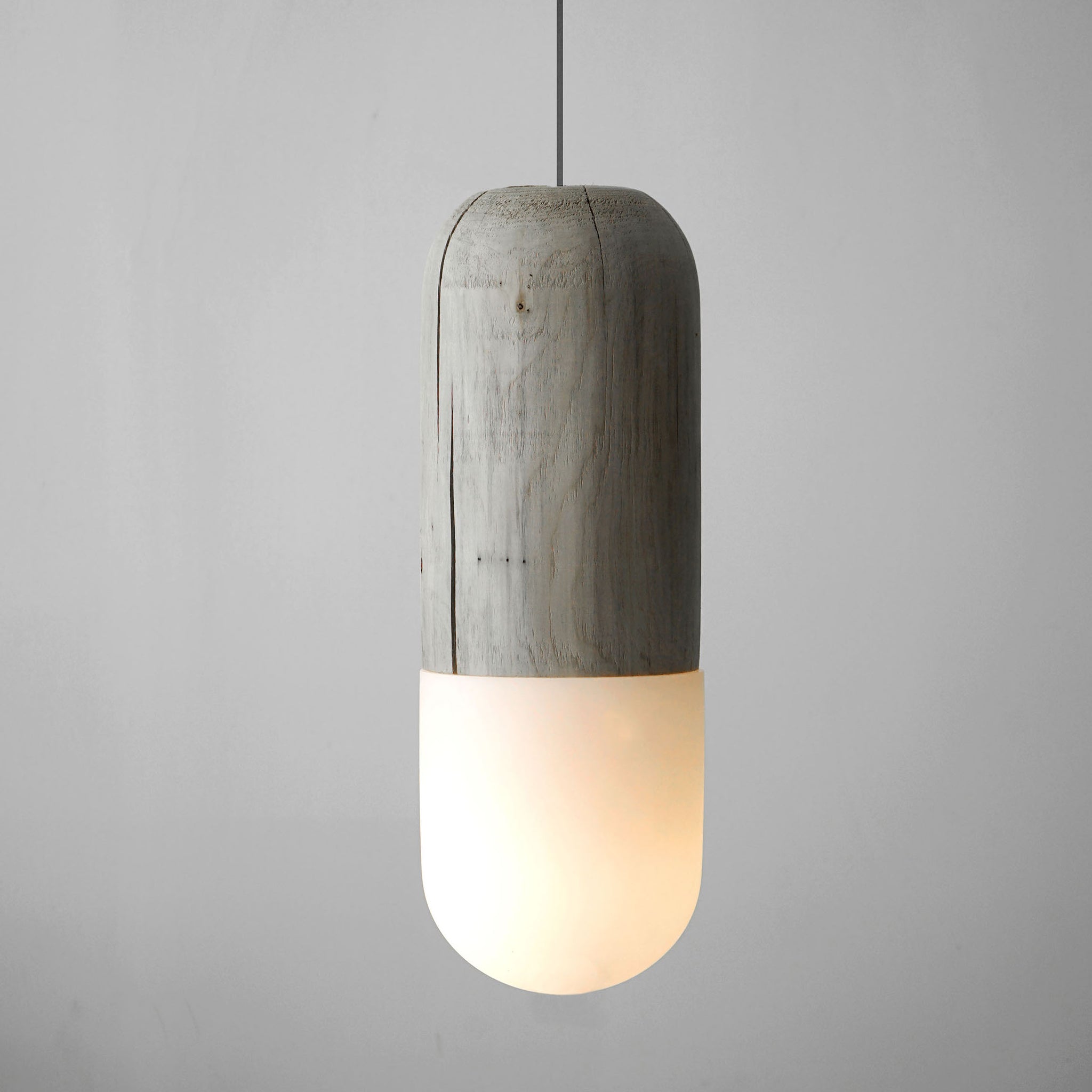 Pendant light made from cedar and handblown glass coming together to form a pill shape