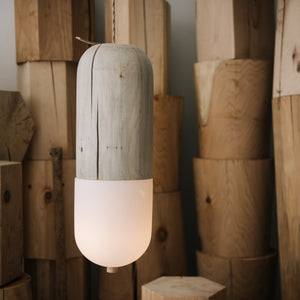 Cedar and handblown glass pendant light suspended in front of various wood stools
