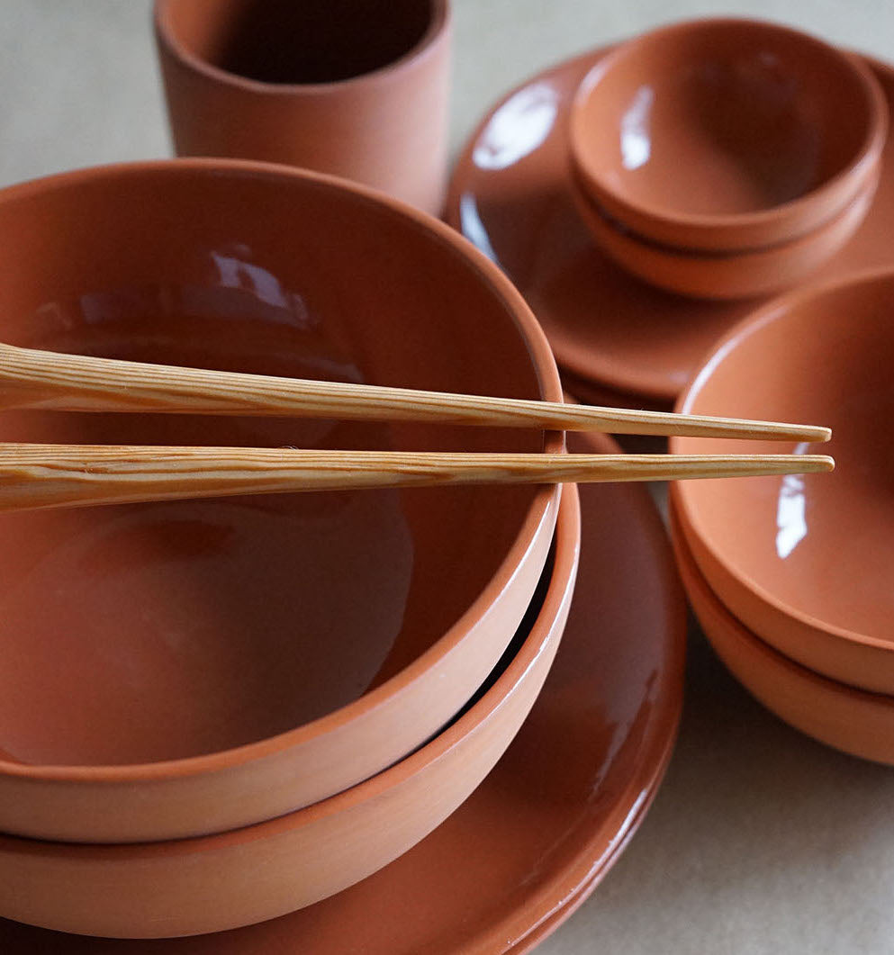hand whittled douglas fir chopsticks laying on a terracotta bowl