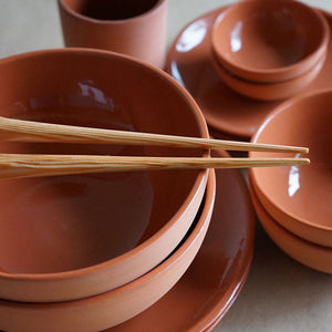 hand whittled douglas fir chopsticks resting on a terracotta bowl