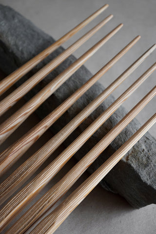 8 hand whittled douglas fir chopsticks laying on a rock