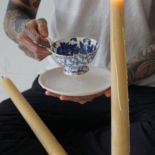 man holding a 6.5" white porcelain side plate and an ornate tea cup