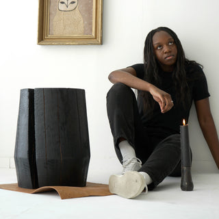 woman sitting next to a solid wood smokestack stool with a charred black finish