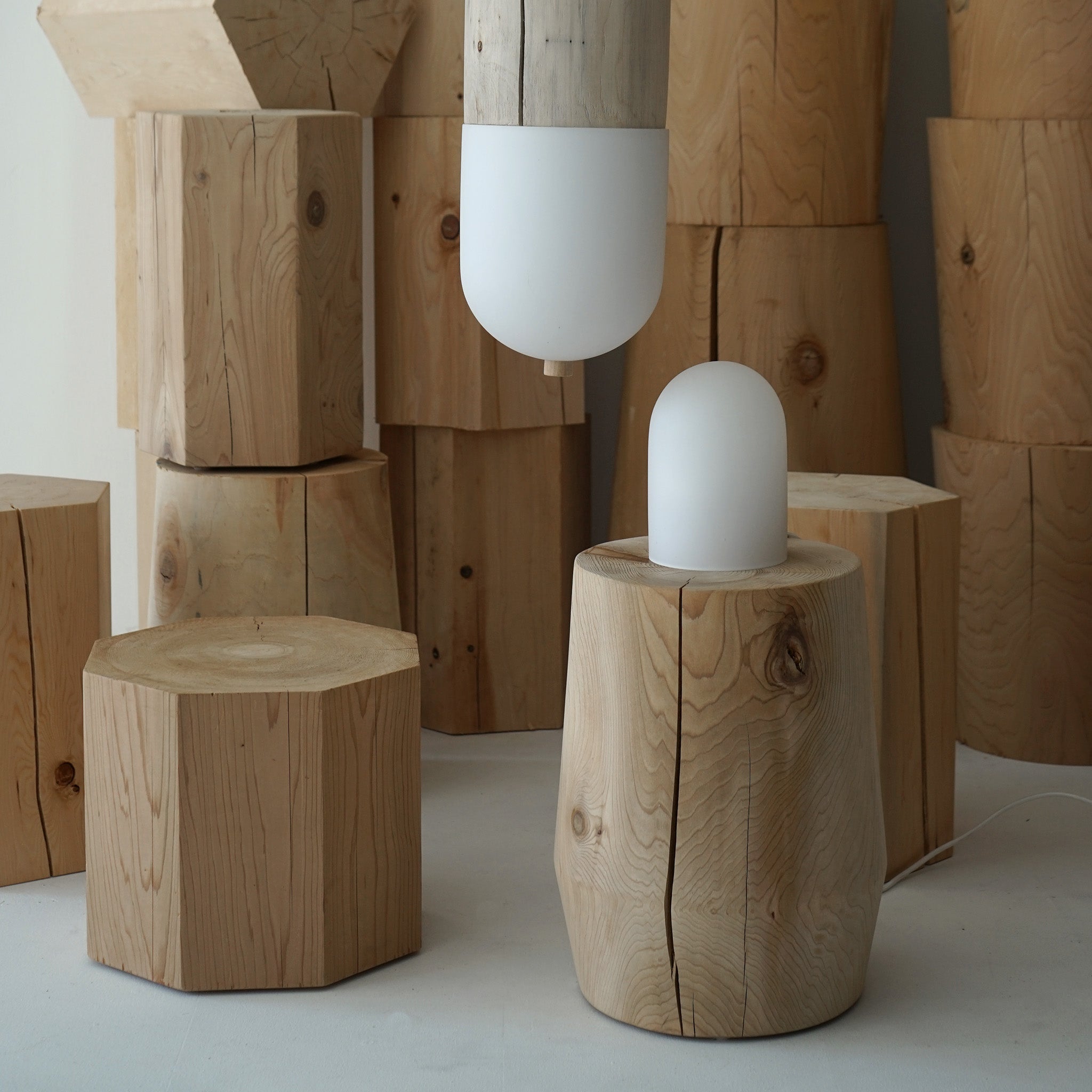 Solid hemlock smokestack stool sitting with various other wood stools with a light on top