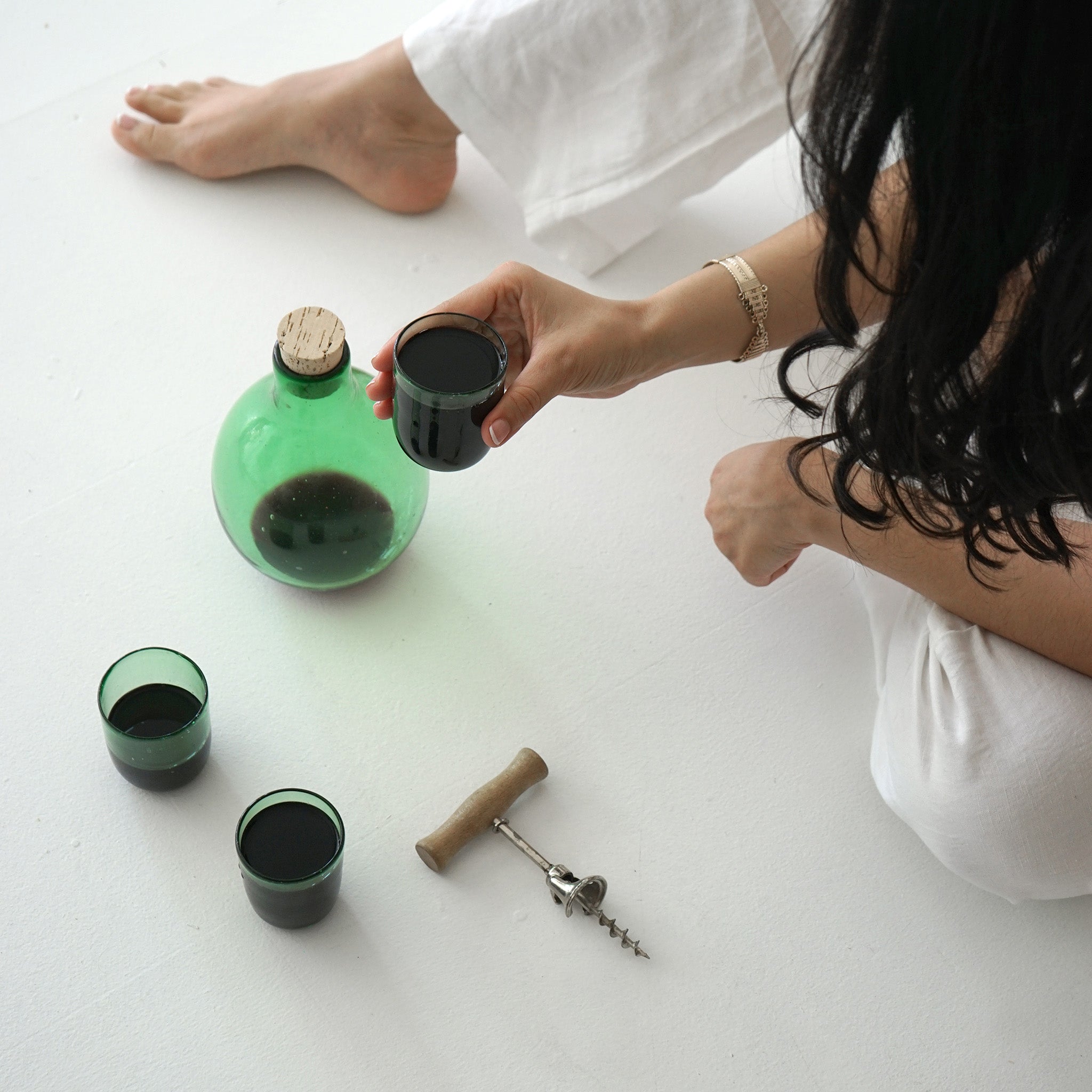 Woman holding a clear green glass cup with the matching pitcher and cup sitting on the floor next to her